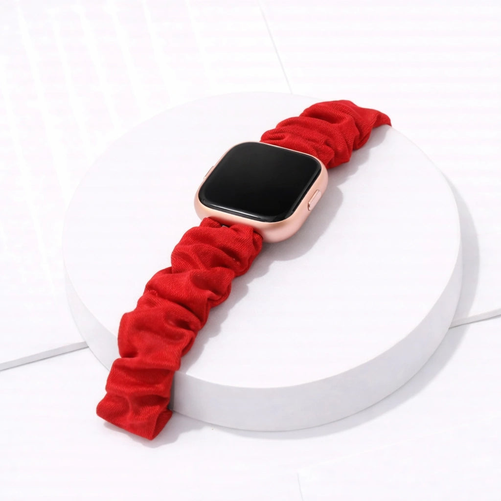 Red fabric scrunchie strap attached to a Fitbit Versa 2 on a white display stand