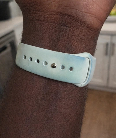 Close-up of a white silicone Apple Watch strap with a greenish tint, worn indoors in a kitchen setting