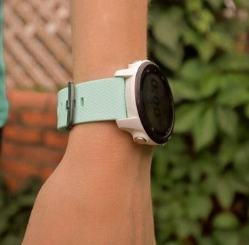 A close-up of a Garmin watch with a mint green strap on a wrist, showing a comfortable skin-safe fit.