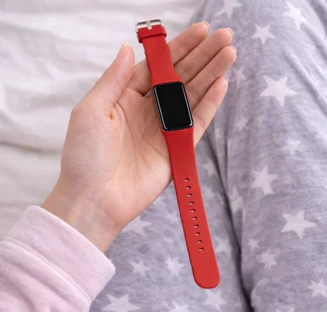 Close-up of red Fitbit Charge 6 band with slim rectangular display, shown in hand with cosy pyjamas for night-time comfort.