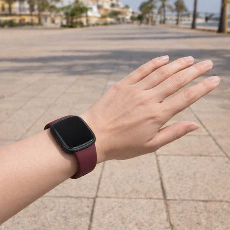 Close-up of a Fitbit Versa 4 with a soft burgundy silicone band worn outdoors, suitable for sensitive skin.