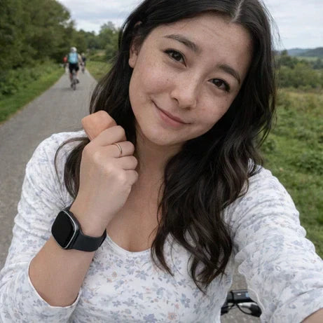 Woman wearing a black Fitbit Versa 4 strap while cycling outdoors, showing how the band fits on the wrist
