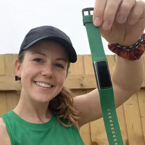 Woman holding a Fitbit Charge 6 green band outdoors, showing the slim tracker design and strap material.