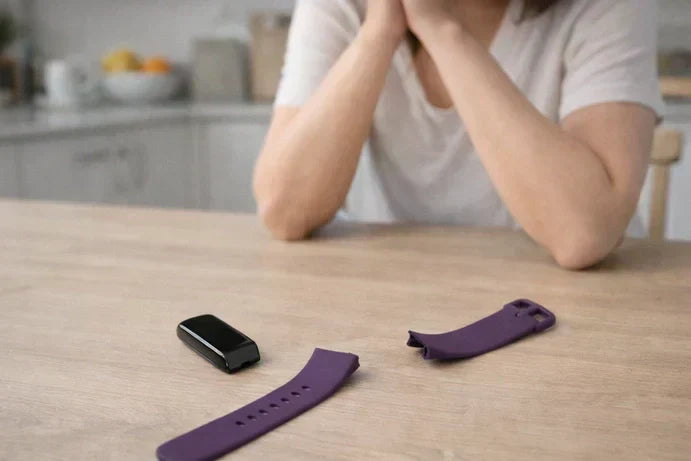 Broken Fitbit Charge 6 strap and tracker placed on a kitchen table as a woman considers whether to repair it.