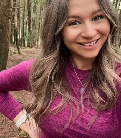 Woman wearing a Fitbit Versa 3 with a white strap while hiking in the woods, smiling at the camera.