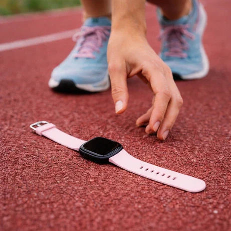 Fitbit Versa 4 lying on a running track after falling off due to an insecure watch band
