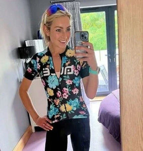 Woman wearing a Fitbit Versa 4 with a mint green strap, taking a mirror selfie in cycling gear. A sporty and stylish example of Fitbit Versa 4 bands for women.
