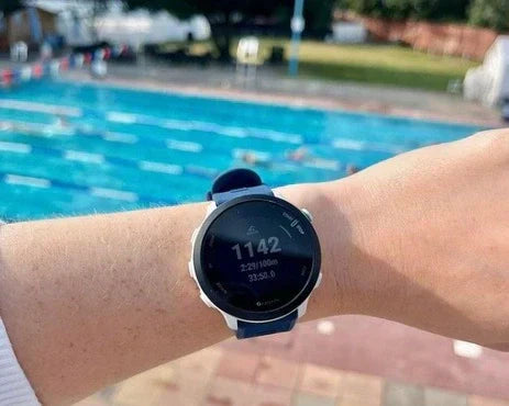 A Garmin watch with a blue waterproof strap being worn near an outdoor swimming pool.