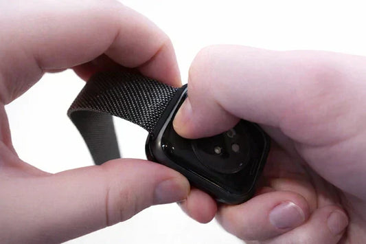 Hands pressing the Apple Watch band release button while sliding the strap out