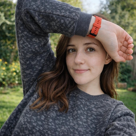 Red silicone Fitbit Charge 6 band suitable for small wrists worn outdoors in a garden.
