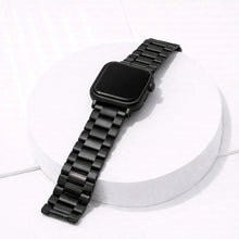 Black stainless steel Apple Watch strap with metal link bracelet design displayed on white stand