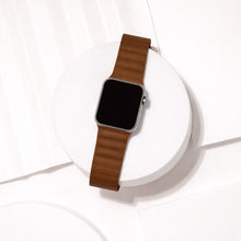 Brown leather Apple Watch strap displayed on a white platform.