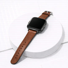 Brown leather strap for Fitbit Versa 2 displayed on a clean studio stand with black watch case.