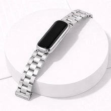 Fitbit Luxe silver metal link watch strap attached to tracker on white display stand