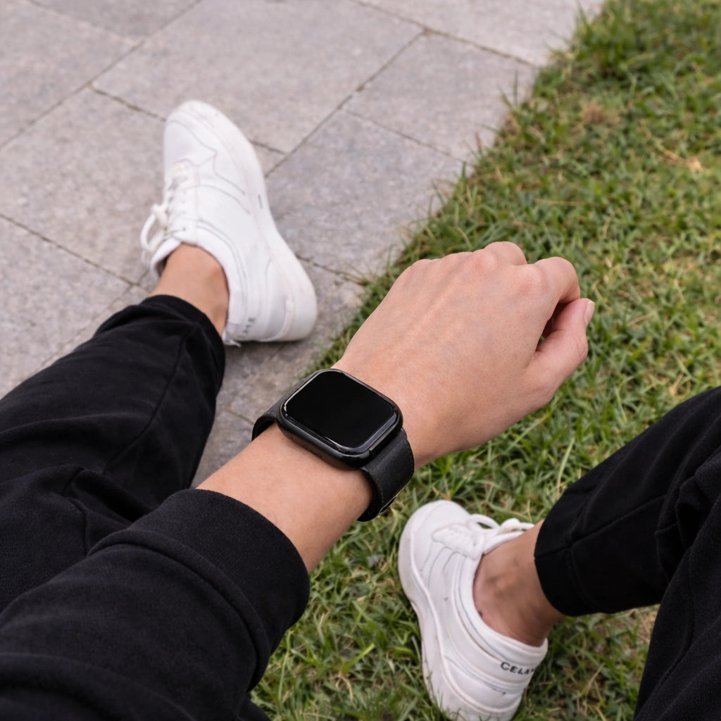 Black leather strap for Fitbit Versa 2 worn outdoors on wrist, shown on pavement and grass