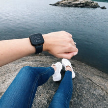Black Fitbit Versa 2 strap worn by the sea in a casual outdoor setting