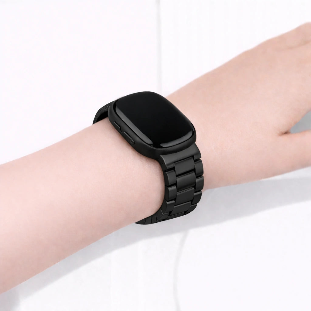 Black stainless steel link band fitted to a Fitbit Versa 3 on the wrist, showing a secure metal bracelet style strap