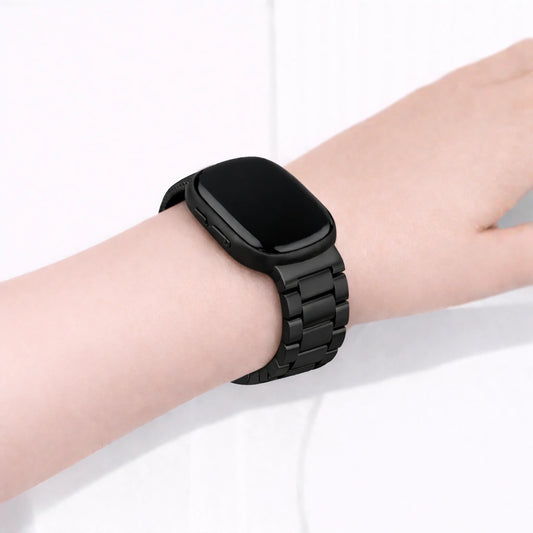 Black stainless steel link band fitted to a Fitbit Versa 3 on the wrist, showing a secure metal bracelet style strap