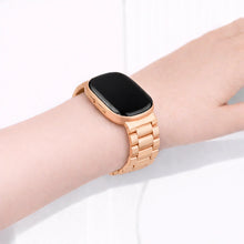 Rose gold stainless steel link band worn on the wrist with a Fitbit Versa 3, featuring a premium metal bracelet design