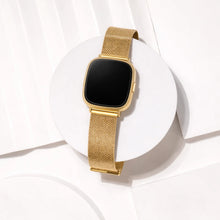 Gold metal strap for Fitbit Versa 4 shown in a minimal studio flat lay