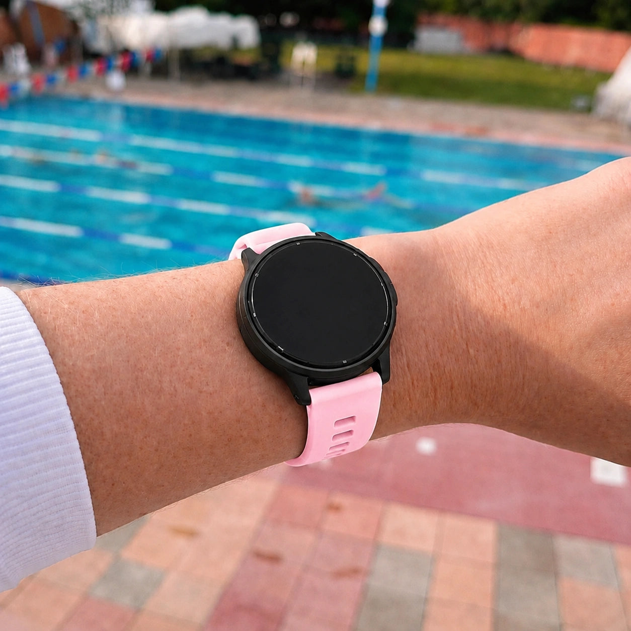Person wearing a light pink Garmin Vivoactive 5 strap beside an outdoor swimming pool