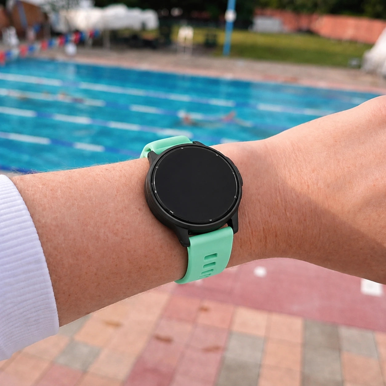Person wearing a mint Garmin Vivoactive 5 strap beside an outdoor swimming pool