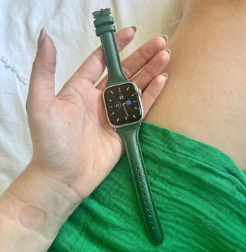 Holding a smartwatch with a green leather strap while relaxing indoors