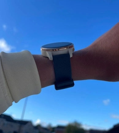 Smartwatch with a black strap worn outdoors under a blue sky