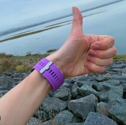 Thumbs up while wearing a purple smartwatch strap by the water